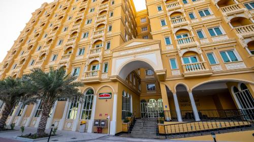 多哈Somerset Al Mansoura Doha的一座黄色的大建筑,前面有棕榈树
