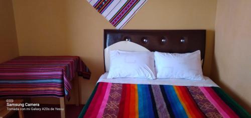 奥科苏尤Paqariy lodge的一张带多色毯子和白色枕头的床