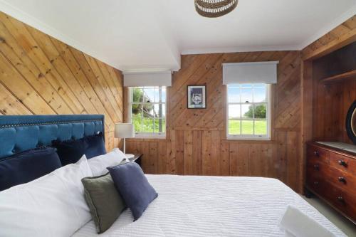 FalmouthWhite Shell Cottage - Woodfire & Beachfront的一间卧室配有一张带蓝色床头板的床和两个窗户