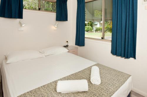 棕榈湾Ellis Beach Oceanfront Holiday Park的一间卧室配有一张带蓝色窗帘的床和一扇窗户