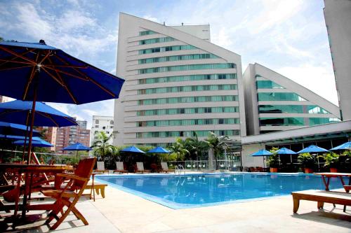 麦德林圣费尔南多广场酒店 的酒店旁的游泳池配有椅子和遮阳伞