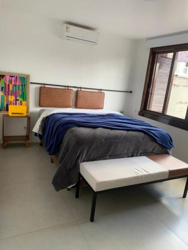 本图贡萨尔维斯Apartamento Artístico - Garagem - Ar Condicionado - Excelente Localização的一间卧室配有一张床、一张长凳和一个窗户。