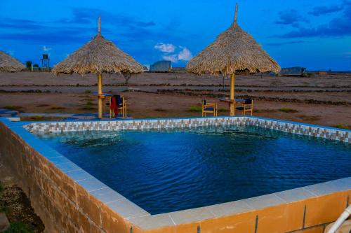安博塞利Amanya King Lion 1-Bed Wigwam in Amboseli的一个带两把稻草遮阳伞的游泳池和一个海滩