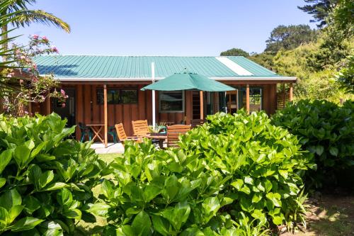 Tryphena大堡礁奥蒂亚洛奇山林小屋的一座带椅子和遮阳伞的绿色屋顶房子