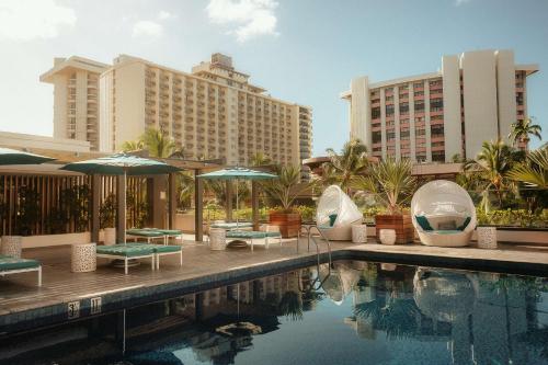 檀香山OUTRIGGER Waikiki Beachcomber Hotel的一个带桌子和遮阳伞的游泳池以及建筑