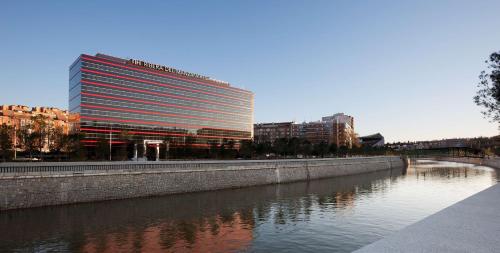 马德里NH马德里里贝拉格兰德曼萨纳雷斯酒店的一座高大的建筑,毗邻一条有建筑物的河流
