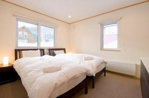 二世古红宝石小木屋的一间卧室配有一张带白色床单的床和两个窗户。