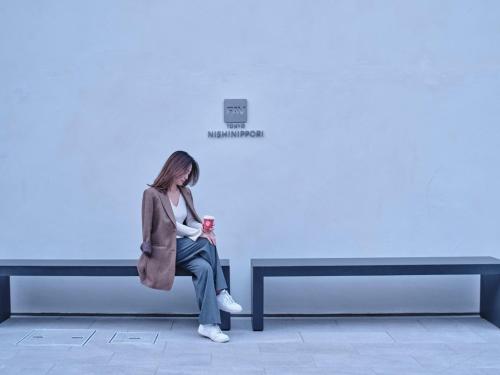 东京FAV TOKYO Nishinippori的坐在长凳上靠墙的女人