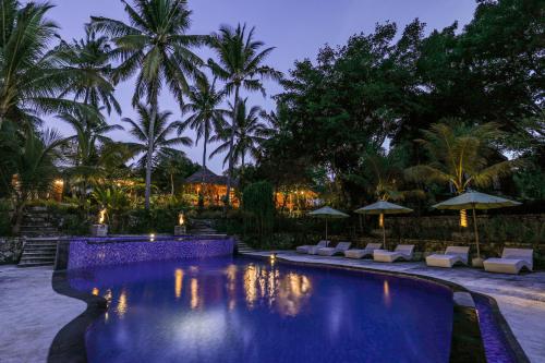 珀尼达岛Bila Penida Resort & Farm的夜间带椅子和遮阳伞的度假游泳池