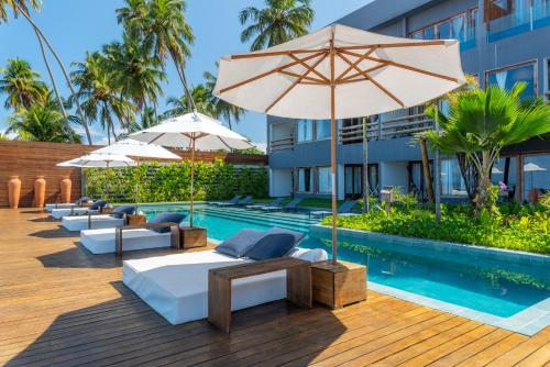 马拉戈日Villa Pantai Boutique Hotel Maragogi的一个带遮阳伞和床的游泳池的度假酒店