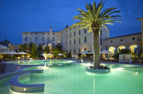 卢特拉艾季普苏赛拉温泉与健身温泉浴酒店的一座大型游泳池,在一座建筑前方有一棵棕榈树