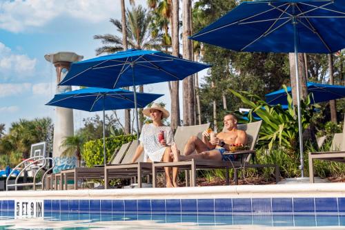 基西米冠军门欧尼酒店的两名妇女坐在游泳池旁的椅子上,旁边配有遮阳伞