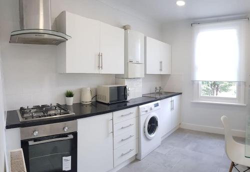 伦敦London. Gorgeous 2 bed flat near Olympic Park.的厨房配有白色橱柜、洗衣机和烘干机