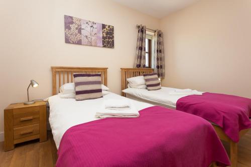 林利斯戈2 Eden at Williamscraig Holiday Cottages的客房内的两张床,上面有粉红色的床单
