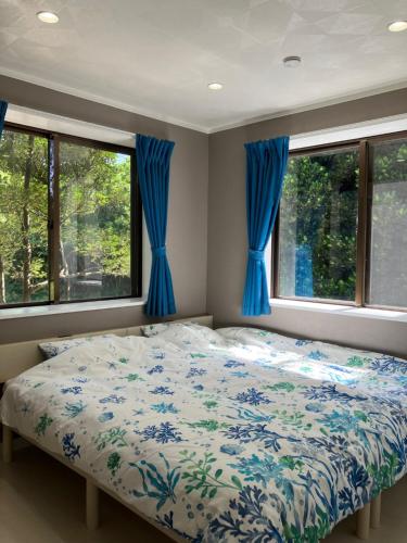 本部Hana Villa 備瀬のや的一间卧室配有一张带蓝色窗帘和窗户的床。