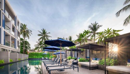 芭东海滩Hotel Indigo Phuket Patong, an IHG Hotel的一座带椅子和遮阳伞的游泳池位于一座建筑旁边