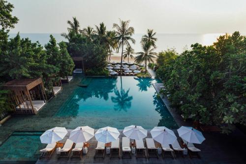 华欣Cape Nidhra Hotel的毗邻大海的带椅子和遮阳伞的游泳池