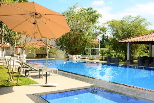 加姆珀哈The Covanro Airport Hotel - Katunayake的游泳池旁的遮阳伞和度假村