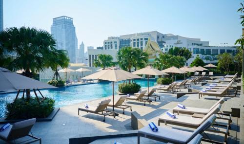 曼谷察殿曼谷大酒店的一座带躺椅和遮阳伞的游泳池,毗邻一个城市