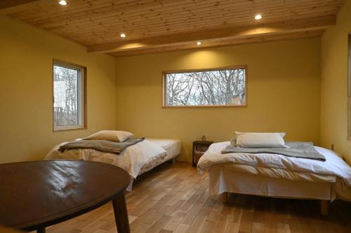 士别市小さな森の貸し切り宿Forest-House-Ranapirica的客房设有两张床、一张桌子和两个窗户。