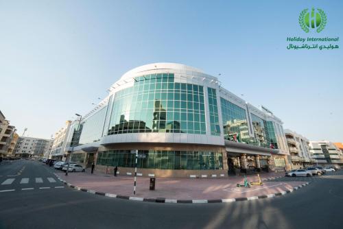 迪拜Holiday International Hotel Embassy District的一座大型玻璃建筑,前面有汽车停放