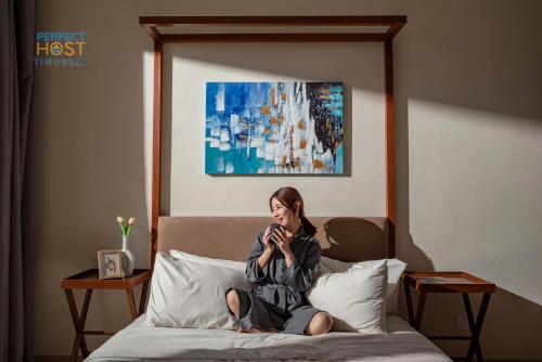 关丹Timurbay Beachfront by Perfect Host的坐在床上的女人在手机上讲话