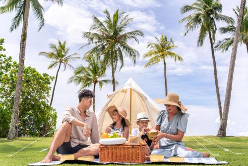蔻立JW Marriott Khao Lak Resort Suites的坐在帐篷前野餐毯上的家庭