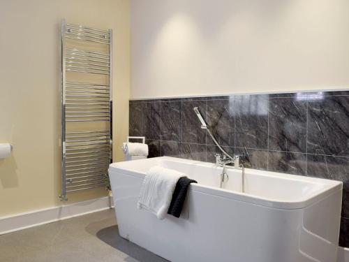 基尔格蒂绿色英亩度假屋的浴室铺有黑色瓷砖,配有白色浴缸。
