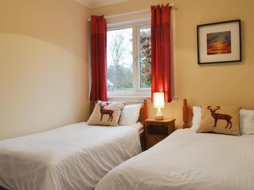 格伦芬南Torr Caladh的配有红色窗帘和窗户的客房内的两张床