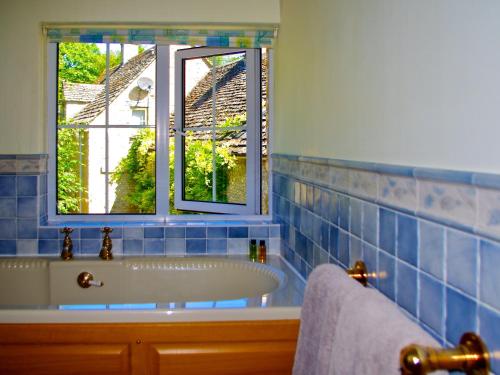 ChedworthIvy Cottage的蓝色瓷砖浴室设有浴缸和窗户。