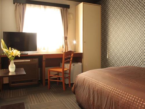 羽村市HOTEL LiVEMAX BUDGET Tokyo Hamura Ekimae的酒店客房配有一张床和一张书桌及一台电视