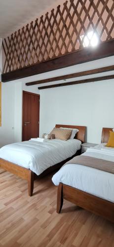 卡米尼亚Casinha da Capela 1935的配有白色墙壁和木地板的客房内的两张床