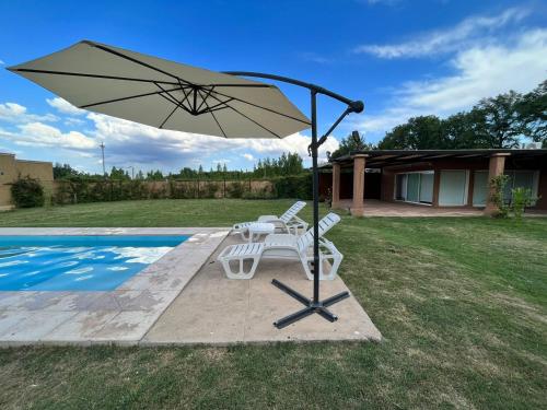 Vista FloresPergolas Guest House - Pileta, Vinos y Montaña的一张桌子和椅子,旁边是游泳池,配有遮阳伞