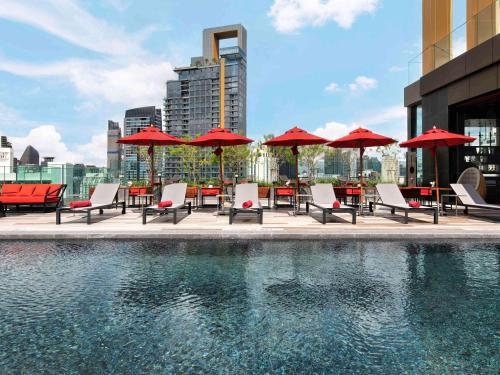 曼谷宜必思尚品曼谷素坤逸4酒店 的一个带桌椅和红色遮阳伞的游泳池