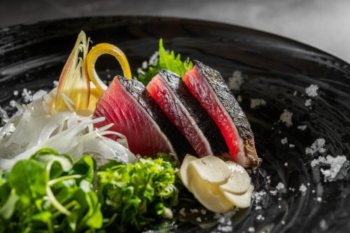 InoKAMENOI HOTEL Kochi的黑盘食物,包括寿司和蔬菜