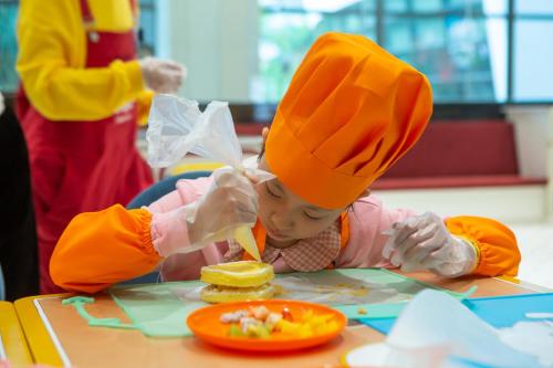 深圳深圳华侨城洲际大酒店的戴着厨师帽的孩子在餐桌上吃食物