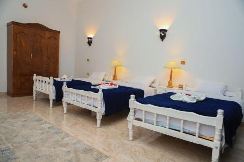 卢克索Luxor Oasis Guest House的一间卧室设有三张床、两张桌子和两盏灯。