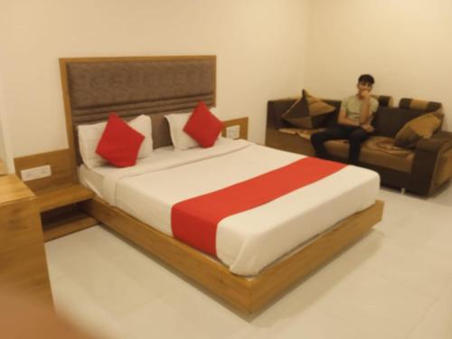 艾哈迈达巴德Hotel Maan Palace的一间卧室配有床,而一个男人坐在沙发上