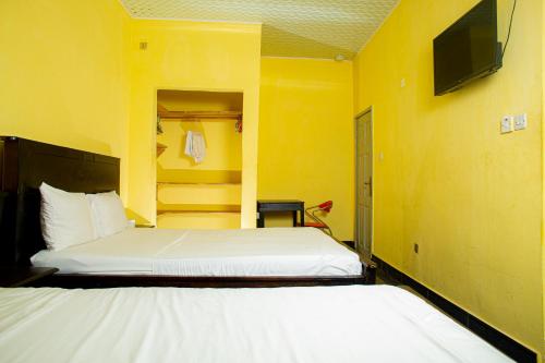 弗里敦Jennabwa Lodge and Restaurant的一间卧室设有两张床,黄色的墙壁上配有电视。