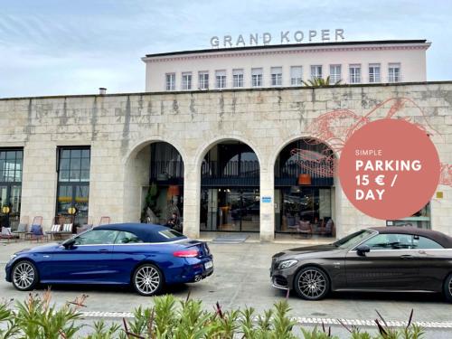 科佩尔Hotel Grand Koper的两辆汽车停在大楼前的停车场