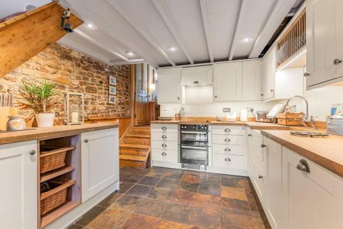 普尔伯勒Pieman's Cottage - Pulborough, West Sussex Cottage - sunny courtyard的厨房配有白色橱柜和石墙