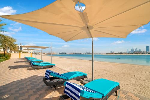 迪拜FAM Living - Sarai Apartments - Private Beachfront Escape in Palm Jumeirah的海滩上一排带遮阳伞的沙滩椅