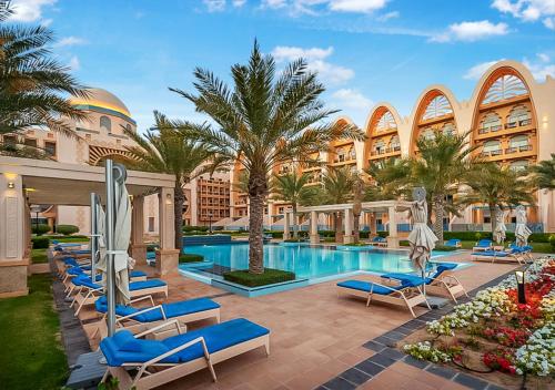 迪拜FAM Living - Sarai Apartments - Private Beachfront Escape in Palm Jumeirah的度假村的游泳池,设有蓝色的躺椅和棕榈树
