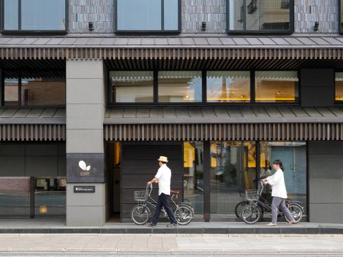 京都Dhawa Yura Kyoto - Banyan Group的两个人在商店前骑着自行车