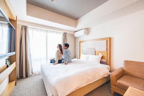 大阪难波大国町瑞利弗酒店的坐在酒店房间床上的男女