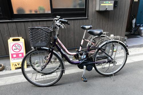 东京無料wi-fi JING HOUSE 秋葉原 電動自転車レンタル的一辆自行车,车上有一个篮子停在建筑物旁边