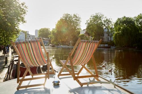 伦敦Boutique Barges的两把椅子坐在池塘前的码头上