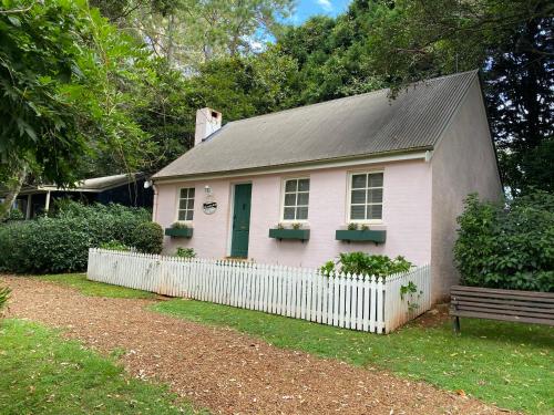 谭伯连山Enchanting Retreat - The English Cottage at Tamborine Mountain的粉红色的小房子,有白色的围栏和长凳
