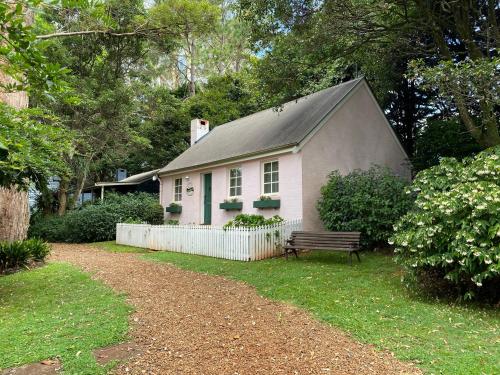 谭伯连山Enchanting Retreat - The English Cottage at Tamborine Mountain的院子内有长凳的小白色房子