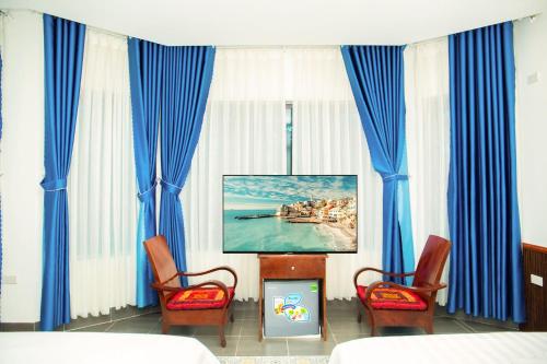 宁平Tam Coc Center Boutique Hotel的一间设有蓝色窗帘、电视和两把椅子的房间